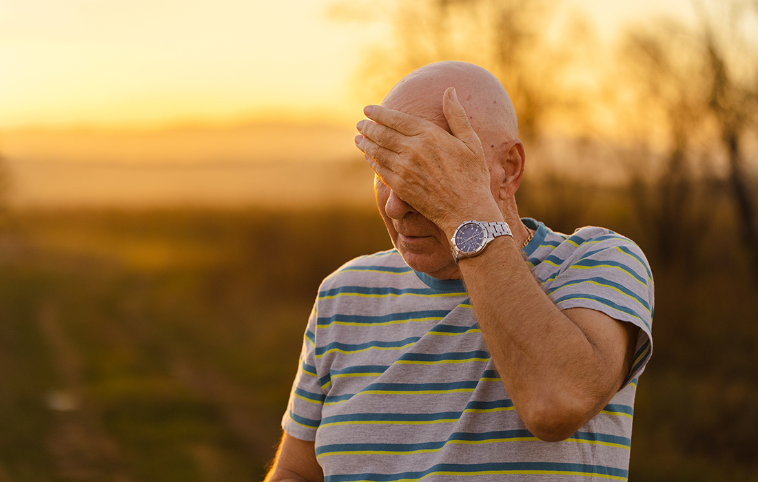 older adults wipes his forehead while walking in nature