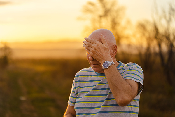 older person wiping forehead while taking a walk outside in nature