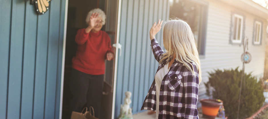 An older woman waving at a caregiver from front door