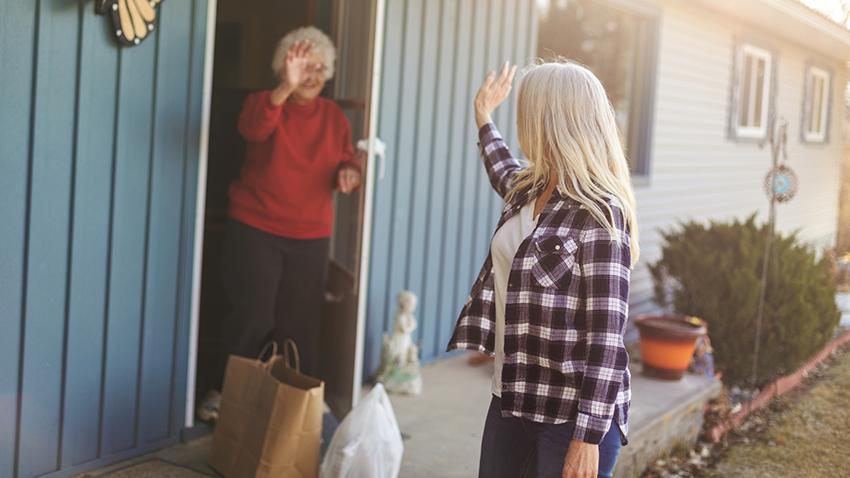 A younger woman dropping off groceries at older woman's home